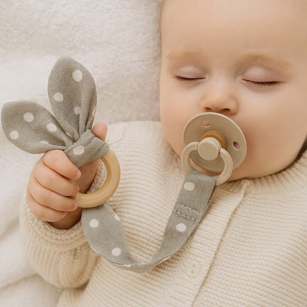 Μωρό κοιμάται κρατώντας υφασμάτινο μασιτικό και κλιπ πιπίλας γκρι πουά με ξύλινο κρίκο