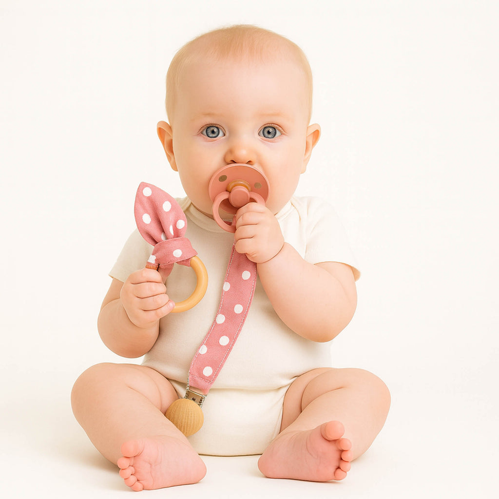 Μωρό κρατά υφασμάτινο μασιτικό και κλιπ πιπίλας σε ροζ πουά χρώμα