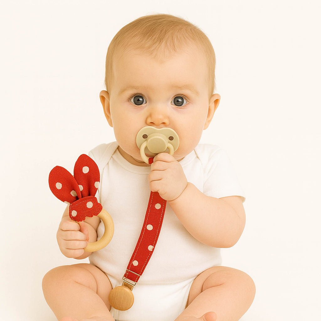 Μωρό κρατάει υφασμάτινο σετ κόκκινο πουά με μασιτικό οδοντοφυΐας και κλιπ πιπίλας με ξύλινο κούμπωμα