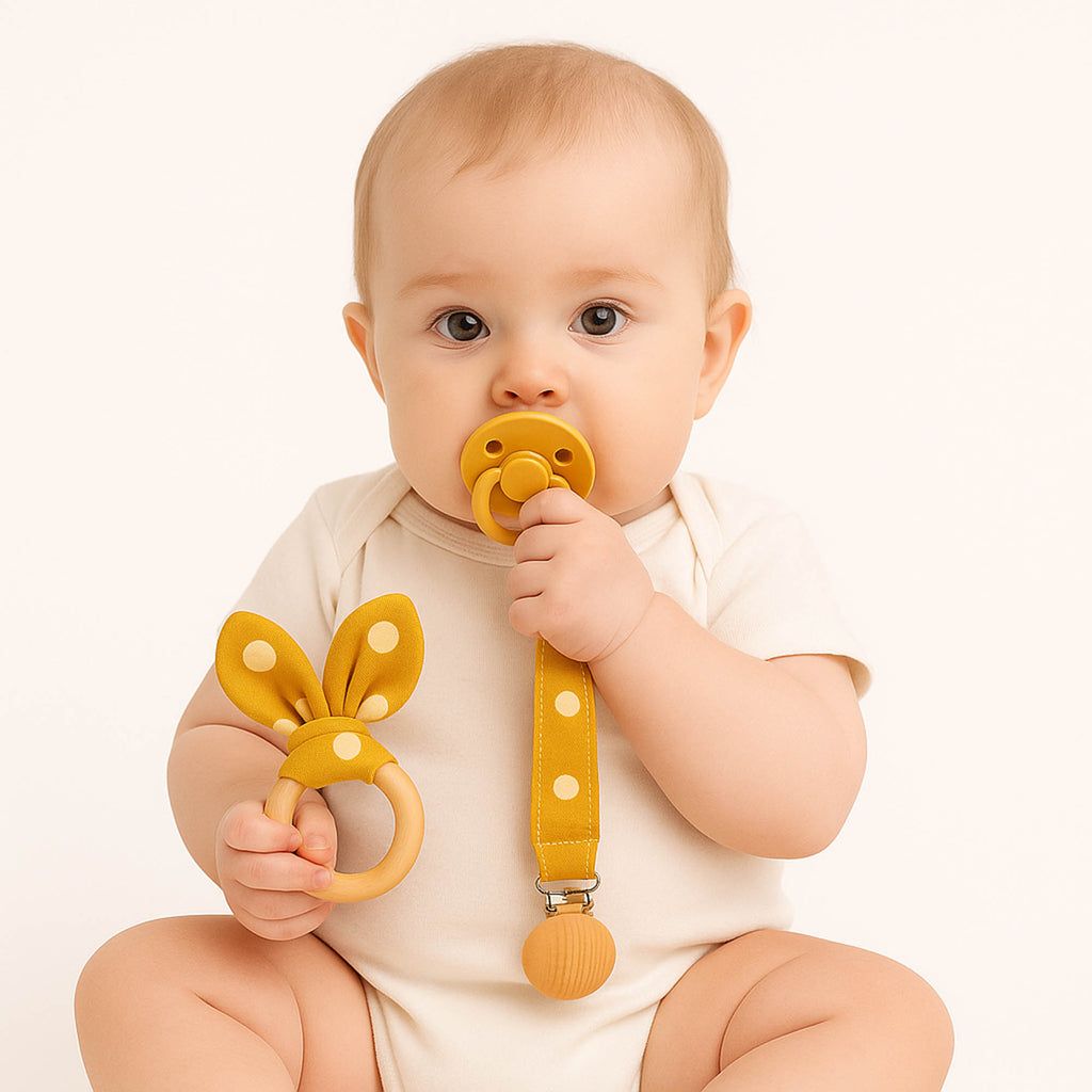 Μωρό κρατά υφασμάτινο μασιτικό και κλιπ πιπίλας σε πουά κίτρινο χρώμα